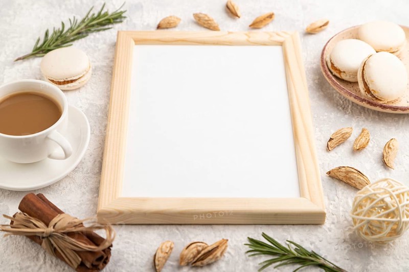 White wooden frame mockup with cup of coffee, almonds and macaroons on gray concrete background. Blank, side view, still life