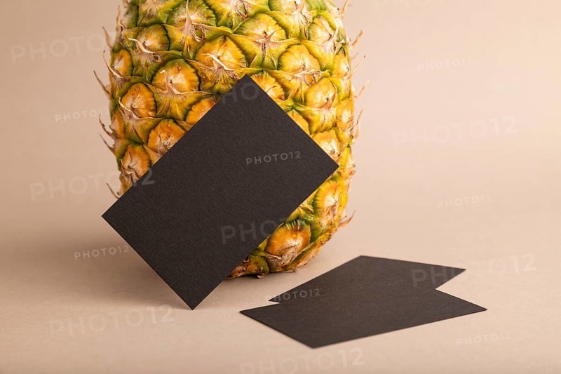 Black paper business card with ripe pineapple on orange pastel background. Side view, copy space. Tropical, healthy food, vacation, holidays concept