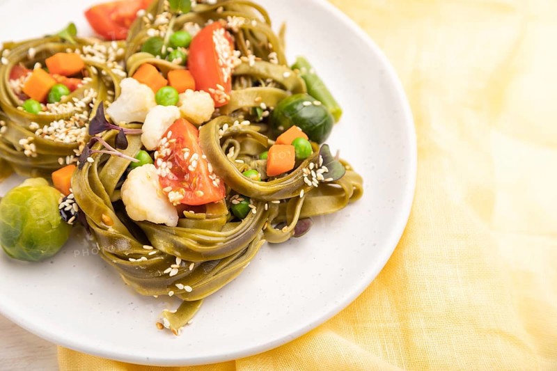 Tagliatelle green spinach pasta with tomato, pea and microgreen sprouts on a white wooden background and yellow textile. Side view, close up, selective focus