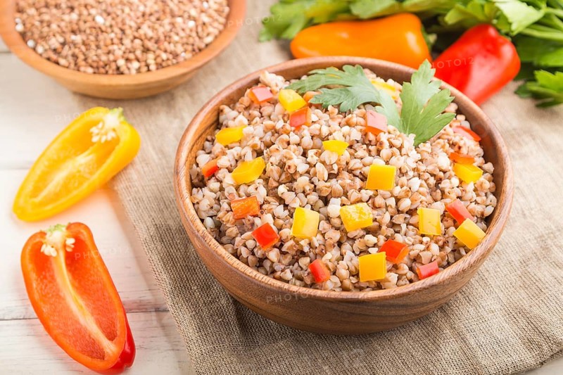 Buckwheat porridge with vegetables in wooden bowl on a white wooden background and linen textile. Side view, close up, selective focus. Russian traditional cuisine