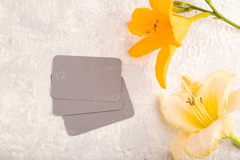 Gray paper business card mockup with orange day-lily flower on gray concrete background. Blank, top view, copy space, still life. spring concept