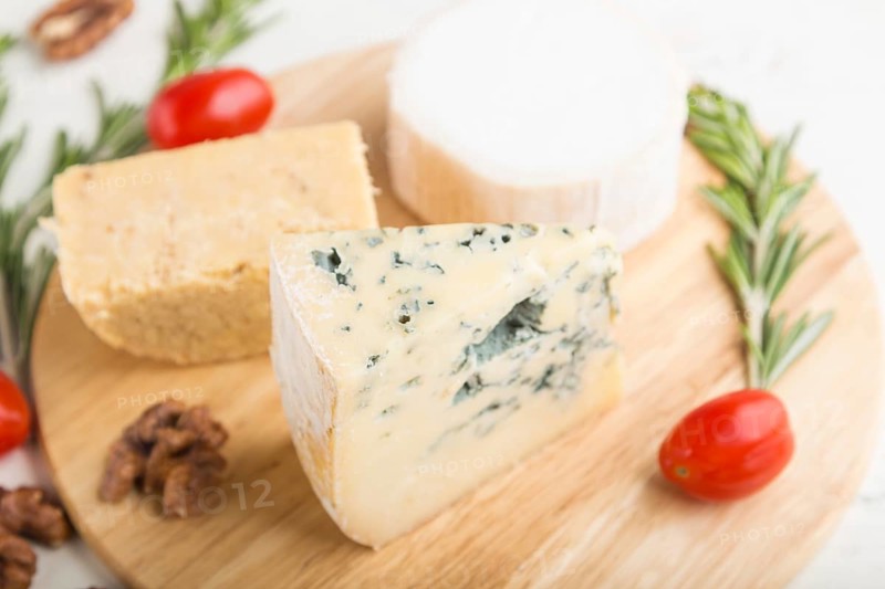 Blue cheese and various types of cheese with rosemary and tomatoes on wooden board on a white wooden background. Side view, close up, selective focus
