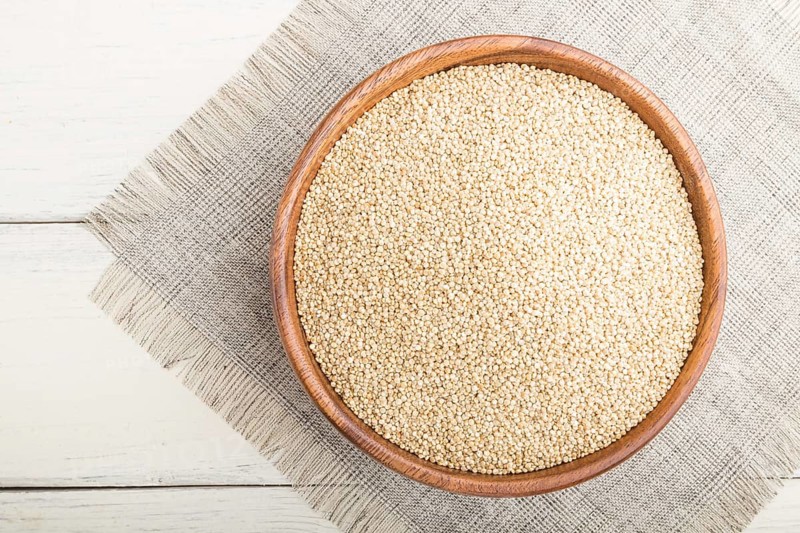 Wooden bowl with raw white quinoa seeds on a white wooden background and linen textile. Top view, flat lay, close up