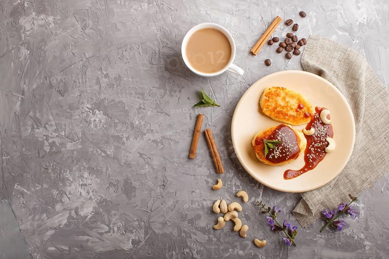 Cheese pancakes with caramel sauce on a beige ceramic plate and a cup of coffee on a gray concrete background. top view, flat lay, copy space