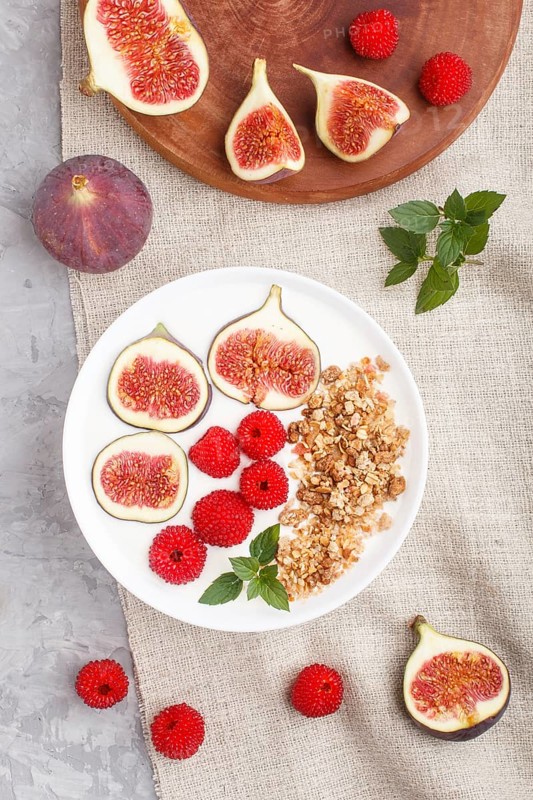 Yoghurt with raspberry, granola and figs in white plate on a gray concrete background and linen textile. top view, flat lay, close up