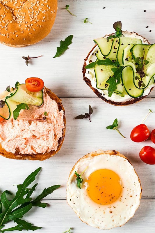 Assortment of sandwiches, white bread, fried egg, cream cheese and cucumber, capelin caviar, sesame bun, breakfast, on a white table, vertical, no people