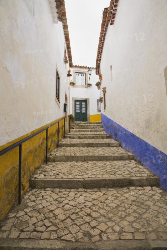 Old street with mosaic style paving stone stairs and white roughcast buildings with blue and yellow painted stripes, Medieval city of Obidos, Portugal, Europe