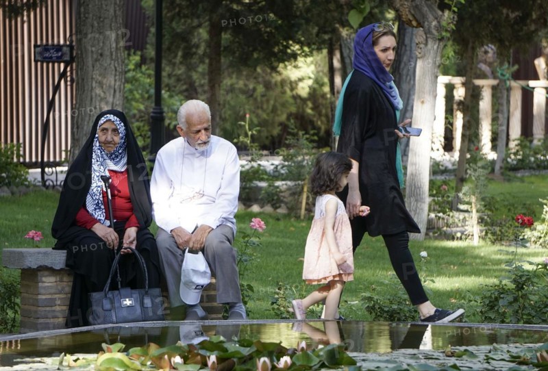 A young Iranian woman walks with her daughter past a traditionally dressed elderly couple sitting on a bench, 22/05/2016