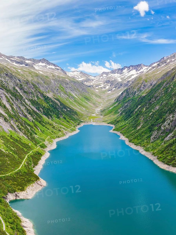 Landscape with a long, blue lake surrounded by high grass and tree-covered hills and snow-capped peaks, Klein Tibet, Zillertal, Austria, Europe