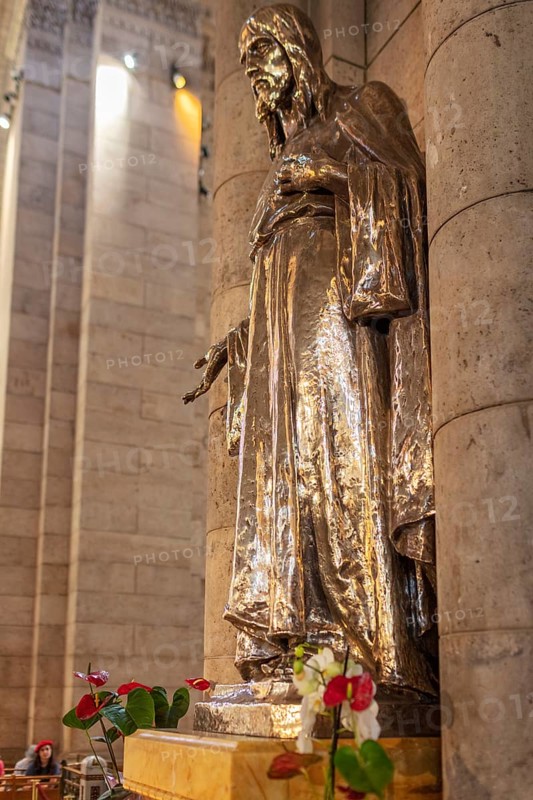 Metal statue in a church, surrounded by flowers, shown in architectural detail, Paris