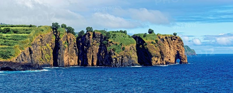 Coastal cliffs looking like a giant elephant with vegetation at the edge of the blue ocean and cloudy sky, Miradouro da Tromba de Elefante, Capelas, Sao Miguel Island, Azores, Portugal, Europe