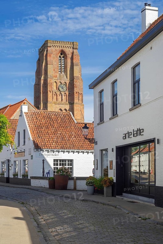 Cobblestone street with restaurant, coffee bar and bell tower of Our Lady's Church at village Lissewege near Bruges in summer, West Flanders, Belgium, Europe
