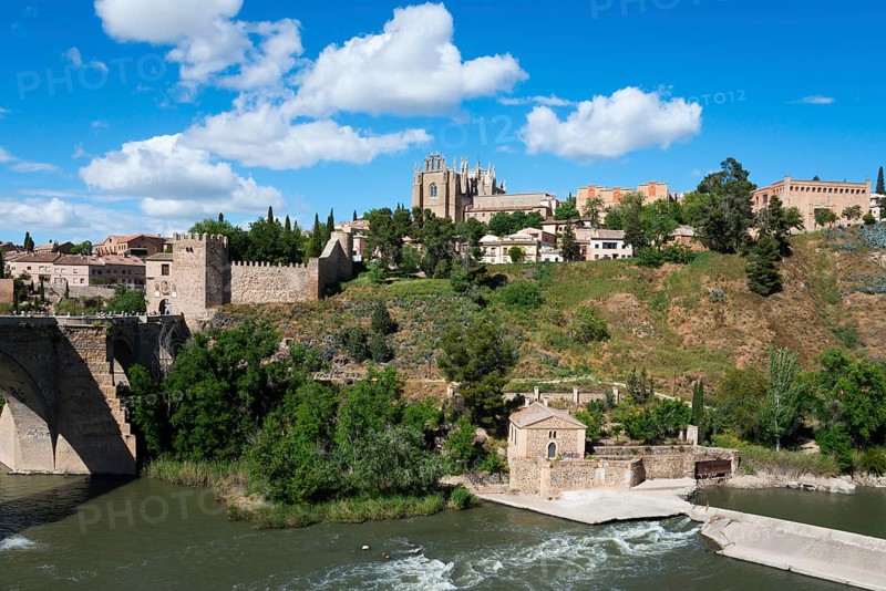 Landscape with river and bridge, in the background a castle and various buildings under a blue sky with clouds, Puente de San Martín, St Martin's Bridge, monastery, Monasterio de San Juan de los Reyes, Toledo, Castilla-La Mancha, Spain, Europe