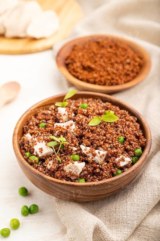 Quinoa porridge with green pea and chicken in wooden bowl on a white wooden background and linen textile. Side view, close up, selective focus
