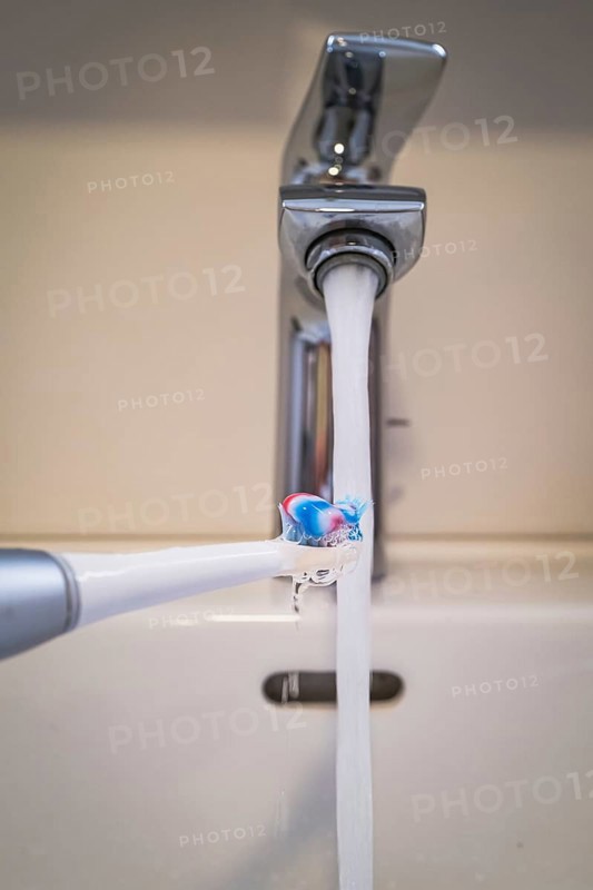 A bathroom tap is running while a toothbrush is held under the running water, symbolic image of water consumption