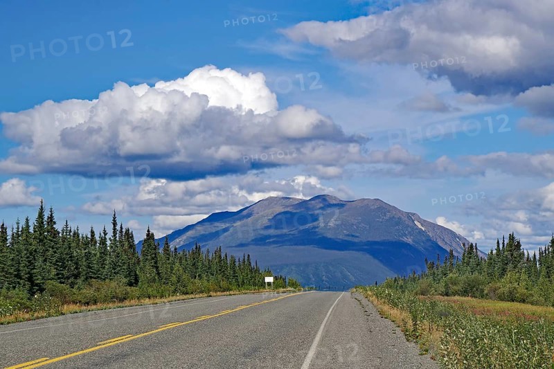 An empty road leads through a picturesque landscape with mountains and clouds in the blue sky, Alaska Highway, Yukon Territory, Canada, North America