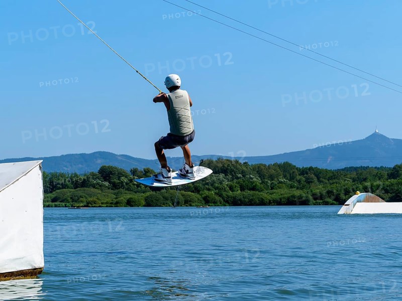 Young man jumping with wakeboard over jump into the lake, water sports, water skiing in wakepark, Stráž pod Ralskem, Czech Republic, Europe