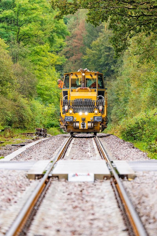 The yellow tractor unit approaches on a railway track, flanked by green forest, Hermann Hesse Bahn track construction, Calw district, Black Forest, Germany, Europe