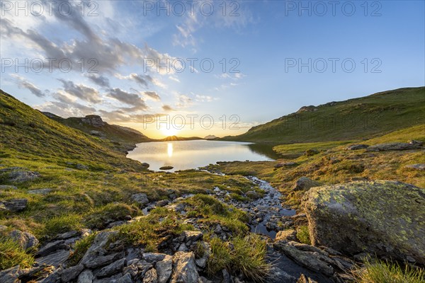 View of a lake at sunrise, surrounded by grassy hills and rocks, Tyrol, Austria, Europe