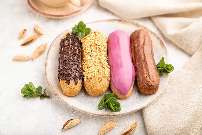Set of eclair, traditional french dessert and cup of coffee on gray concrete background and linen textile. side view, close up, selective focus, still life. Breakfast, morning, concept