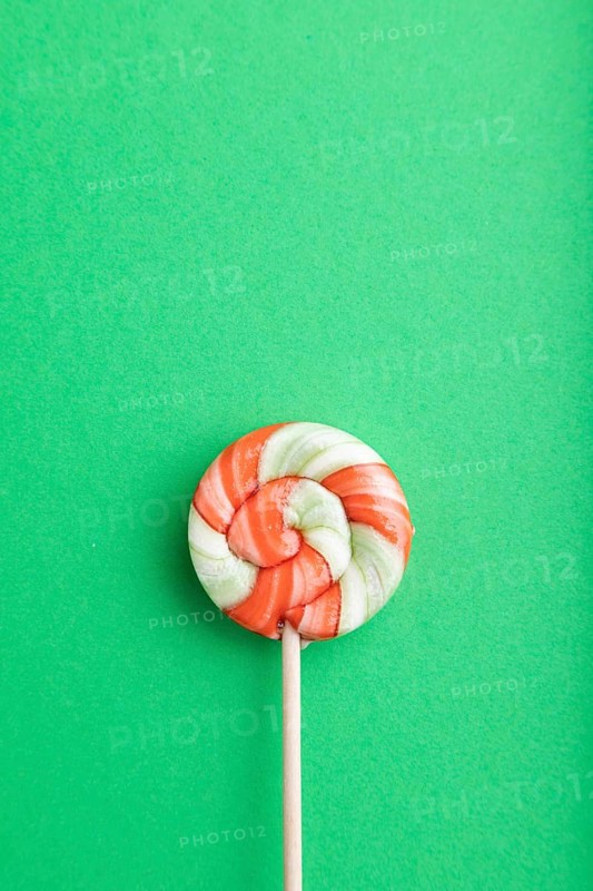 Single lollipop candy on green pastel background. copy space, top view, flat lay