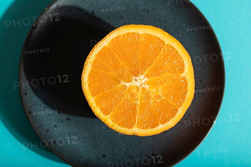 Ripe cut orange on blue ceramic plate on blue pastel background. Top view, flat lay, close up, hard light. Tropical, healthy food, concept, minimalism