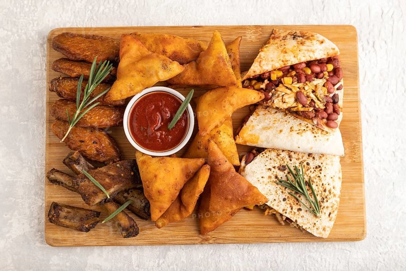 Set of snacks: nachos, chicken wings, fried ribs, bean tortillas on a cutting board on a gray concrete background. Top view, flat lay, close up