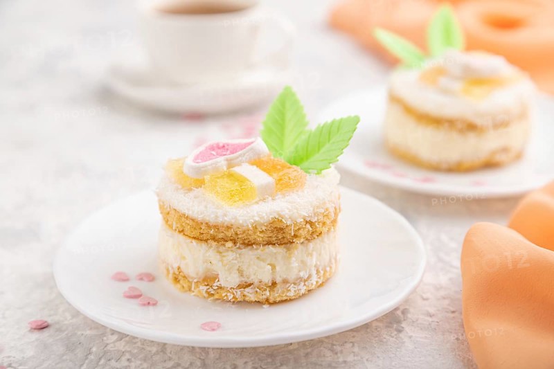 Decorated cake with milk and coconut cream with cup of coffee on a gray concrete background and orange textile. Side view, close up, selective focus