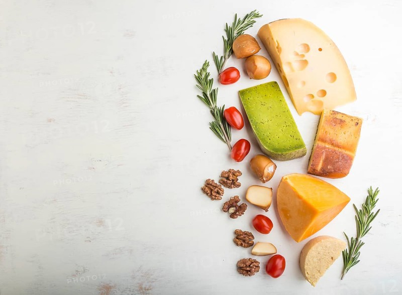 Set of different types of cheese with rosemary and tomatoes on a white wooden background. Top view, flat lay, copy space