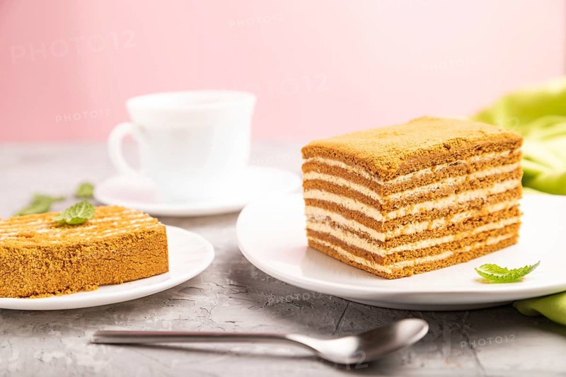 Homemade honey cake with milk cream and mint with cup of coffee on a and pink background and green textile. Side view, close up, selective focus