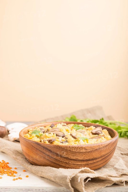Lentils porridge with champignons and coriander in a wooden bowl on a white and orange background and linen textile. Side view, close up, selective focus