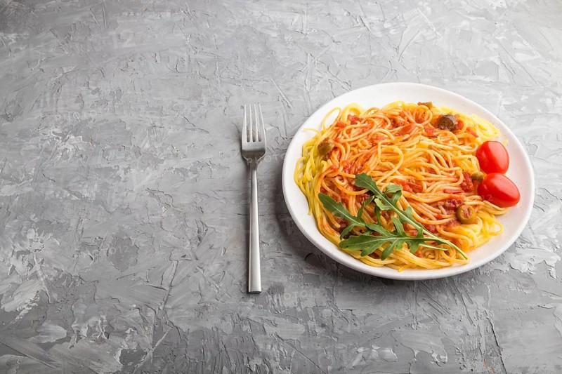 Corn noodles with tomato sauce and arugula on a gray concrete background. Side view, close up, copy space