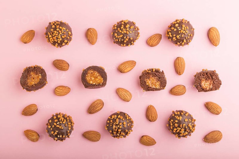 Chocolate caramel ball candies with almonds in a row on a pastel pink background. top view, flat lay
