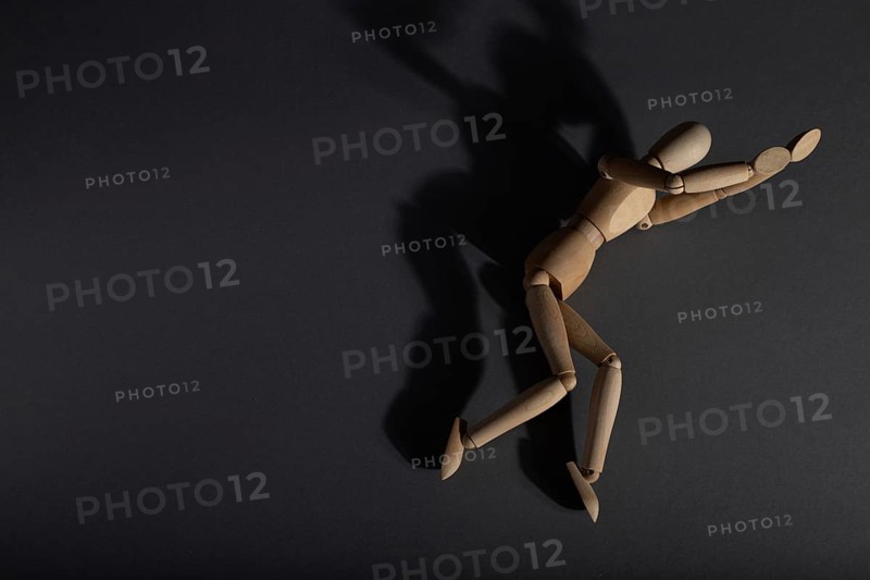 Wooden mannequin lies in a protective position on gray background. loneliness, violence, vulnerability, depression disorder concept. copy space, hard light