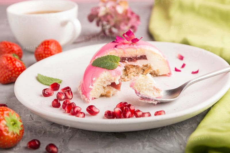 Pink mousse cake with strawberry and a cup of coffee on a gray concrete background and green textile. side view, close up, selective focus, bitten off