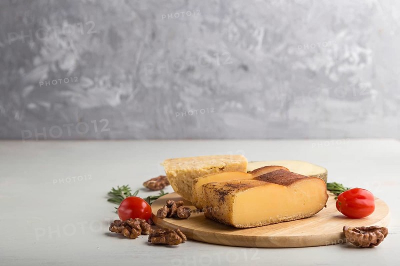 Smoked cheese and various types of cheese with rosemary and tomatoes on wooden board on a gray and white background. Side view, copy space, selective focus