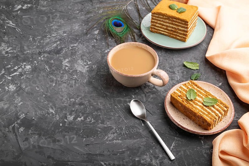 Homemade honey cake with milk cream and mint with cup of coffee on a black concrete background and orange textile. Side view, copy space