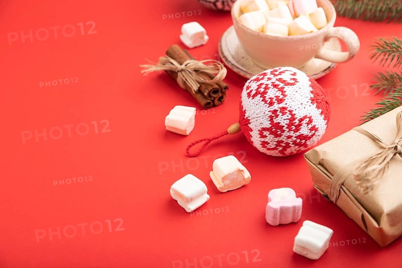 Christmas or New Year composition. Decorations, box, cinnamon, knitted balls, fir and spruce branches, cup of coffee, on a red paper background. Side view, copy space, selective focus