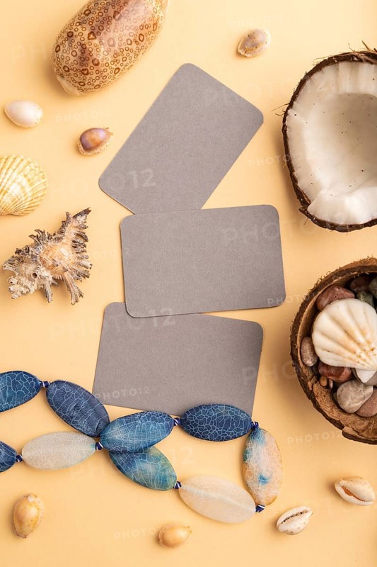 Brown paper business card with coconut, seashells, pebbles, beads on orange pastel background. Top view, flat lay, copy space. Tropical, healthy food, vacation, holidays concept
