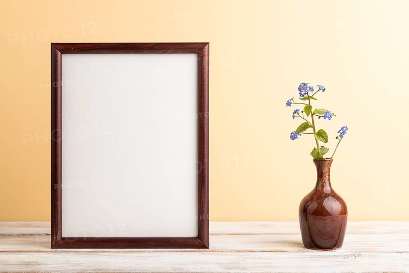 Wooden frame with blue forget-me-not flowers in ceramic vase on orange pastel background. side view, copy space, still life, mockup, template, spring, summer minimalism concept