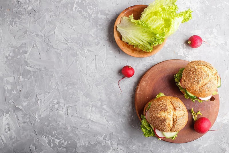 Sandwiches with cheese, radish, lettuce and cucumber on wooden board on a gray concrete background. top view, copy space