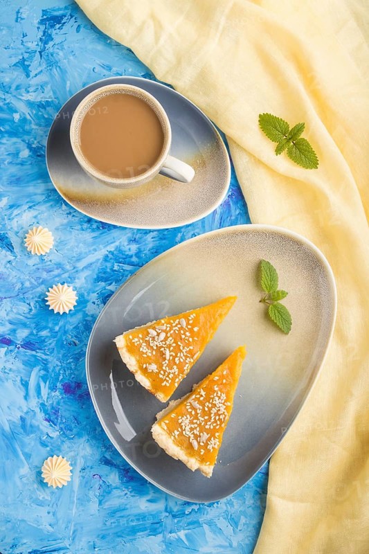 Two pieces of traditional american pumpkin pie with cup of coffee on a blue concrete background and yellow textile. top view, flat lay, close up, contrast