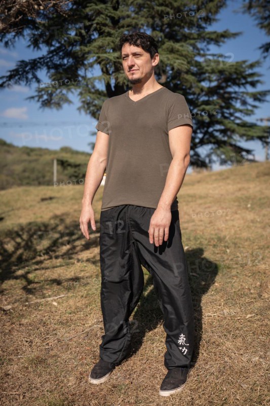 A man outdoors adopts the Wu Chi posture, known as The Void, which marks the beginning of his qi gong or chi kung training session