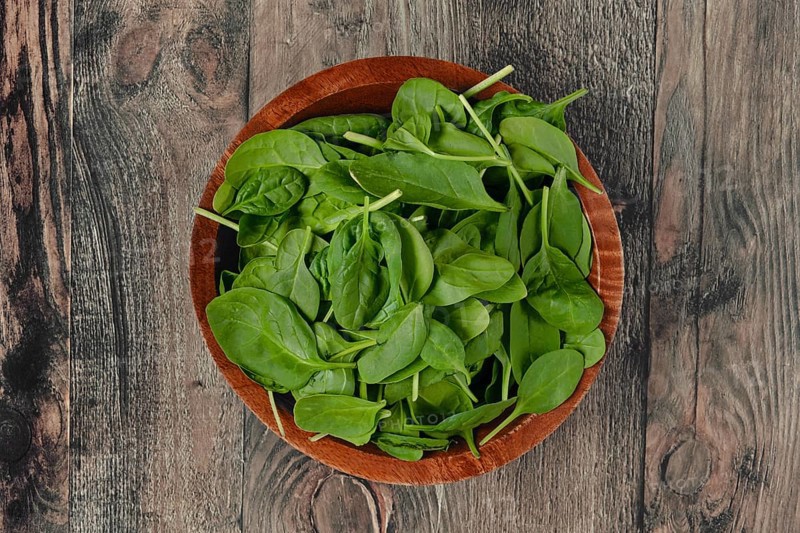 A wooden bowl with vibrant, fresh and crisp spinach leaves on a rustic wooden table, ideal for preparing healthy meals or adding to salads