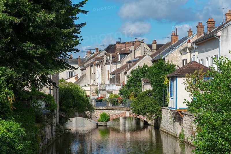 Malerisches Dorf mit Fluss, Brücke und dichten Häusern, umgeben von viel Grün und blauem Himmel, Nemours am Fluss Loing, Département Seine-et-Marne, Region Île-de-France, Ile-de-France, Frankreich