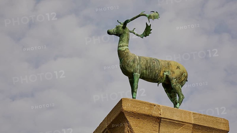 A bronze deer statue on a pedestal in front of a blue sky with clouds, Mandraki harbour, harbour area, Rhodes town, Rhodes, Dodecanese, Greek Islands, Greece, Europe