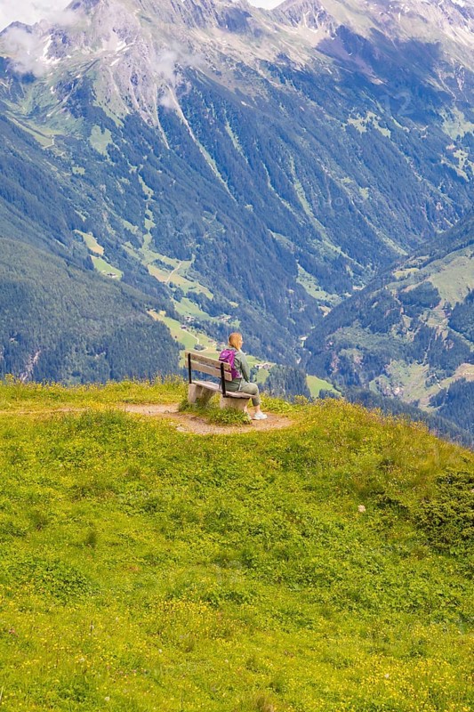 A woman sits on a bench and observes the sweeping valleys and green hills, Penken, Zillertal, Austria, Europe