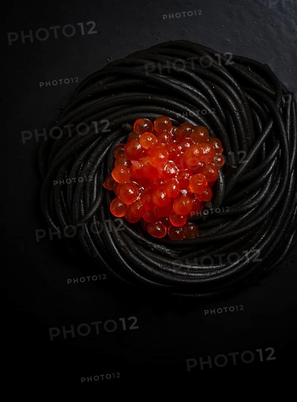 Black spaghetti with red caviar, pasta, on a black background, top view, no people