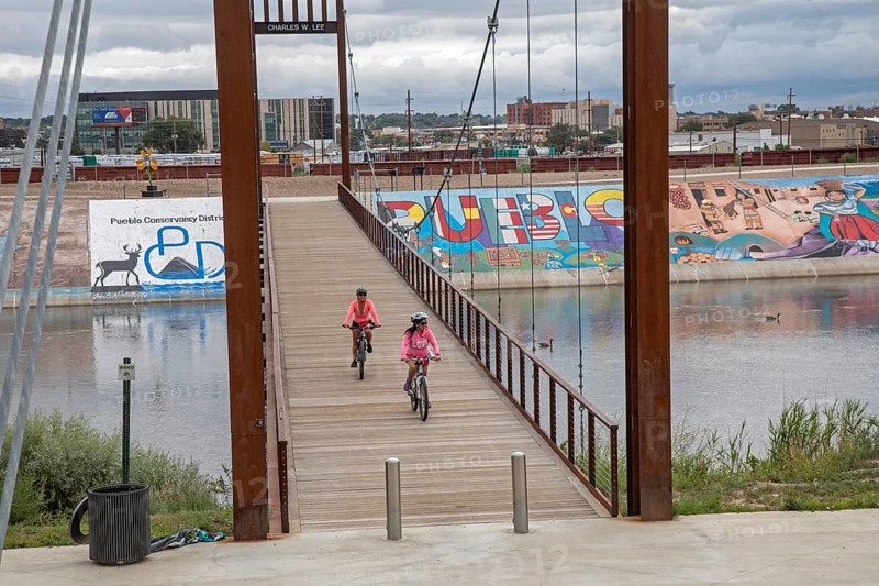 Pueblo, Colorado, Bicycle riders cross a bridge over the Arkansas River where murals and a bike path line the levee. The levee was built after a disastrous 1921 flood. Students painted unauathorized murals in the 1970s, but the artwork has since become accepted as the Pueblo Levee Mural Project