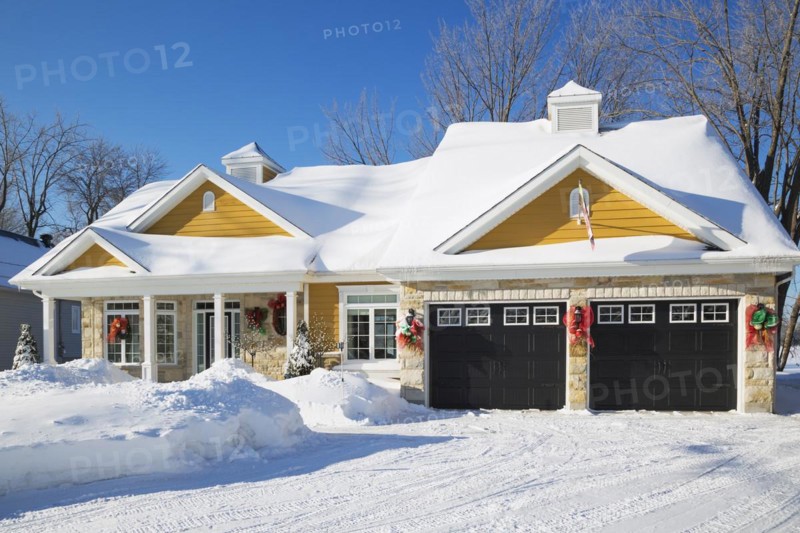 Beige and tan natural cut stone with yellow wood cladding, white and black trim country style house facade in winter, Quebec, Canada, North America